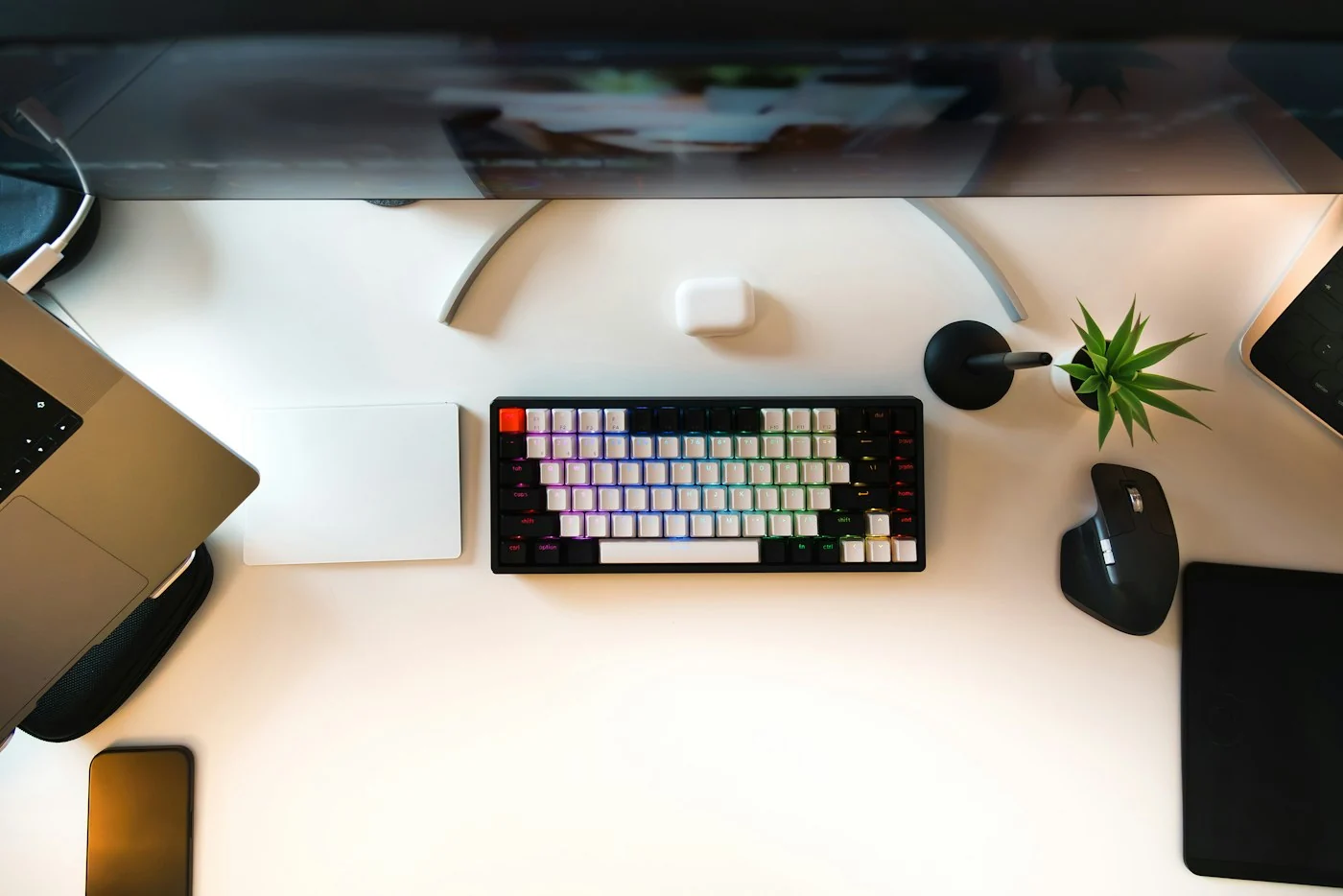 A desk seen from above with a laptop, a compact keyboard, a black mouse and a small plant