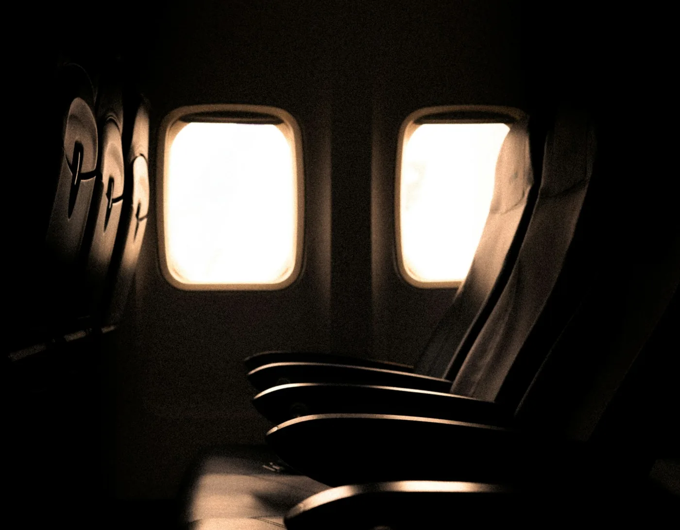 Dim airplane cabin with empty seats and two bright windows letting in light