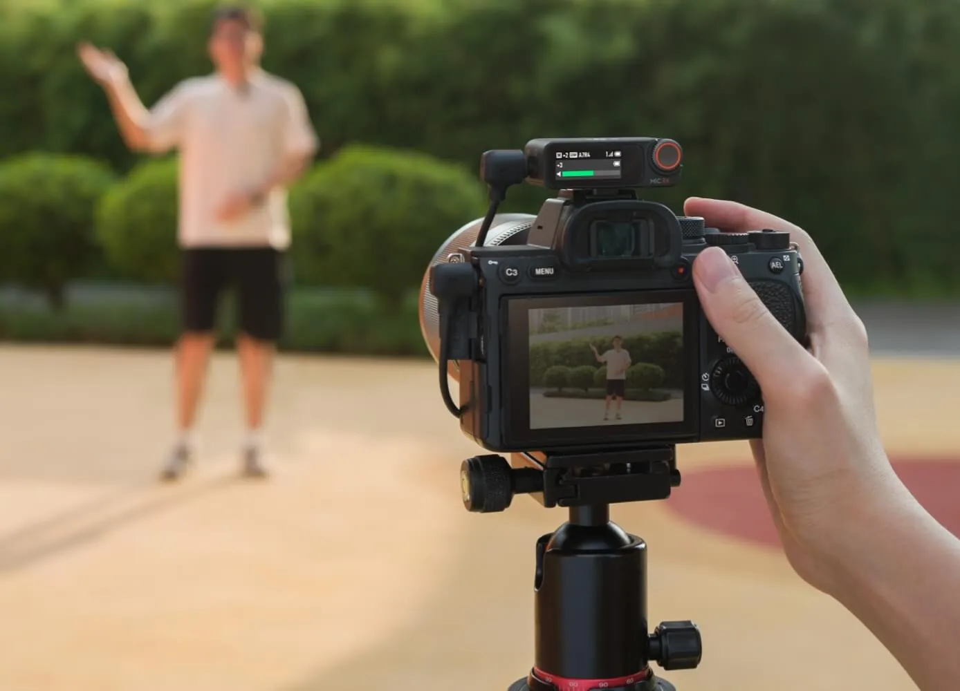 Hand holding a camera on a tripod with a DJI Mic 2 receiver on top while recording a person outdoors