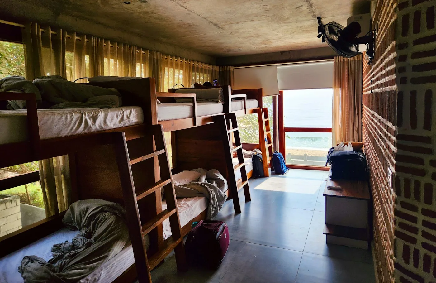 Hostel dorm room with wooden bunk beds and a window with a view of the sea