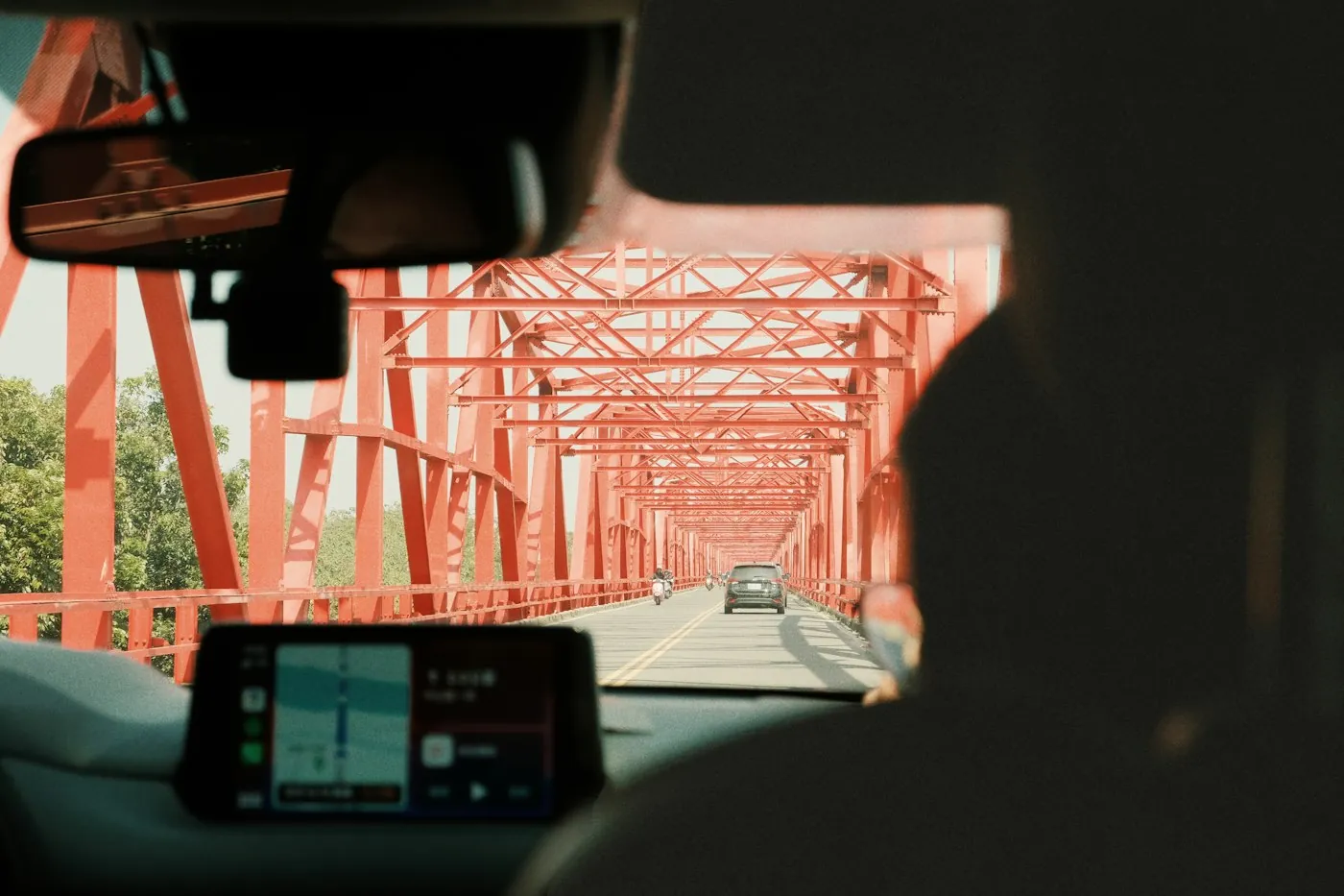 Blick vom Rücksitz eines Autos, das über eine rote Stahlbrücke fährt, mit einem Navigationsbildschirm auf dem Armaturenbrett