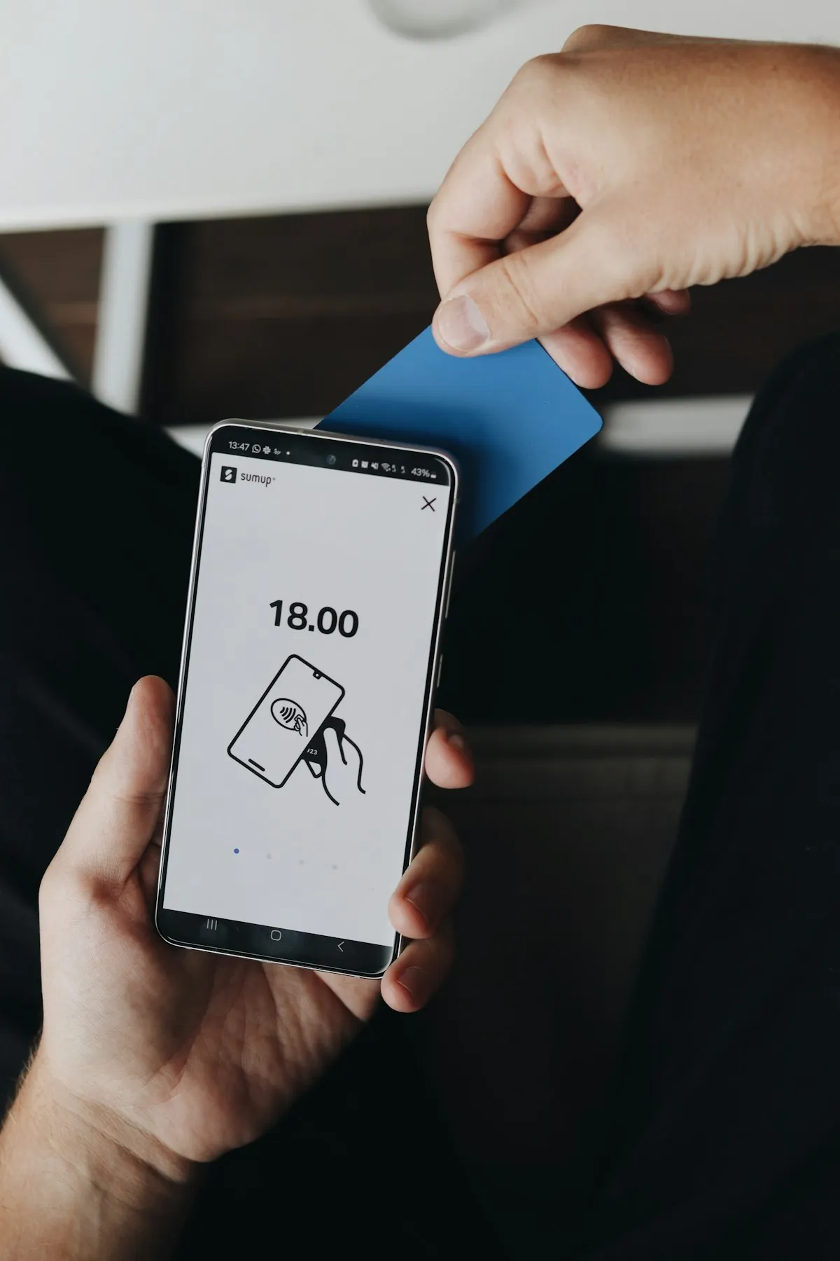 Hand holding a blue card over a phone showing a payment amount, dynamic currency conversion choice