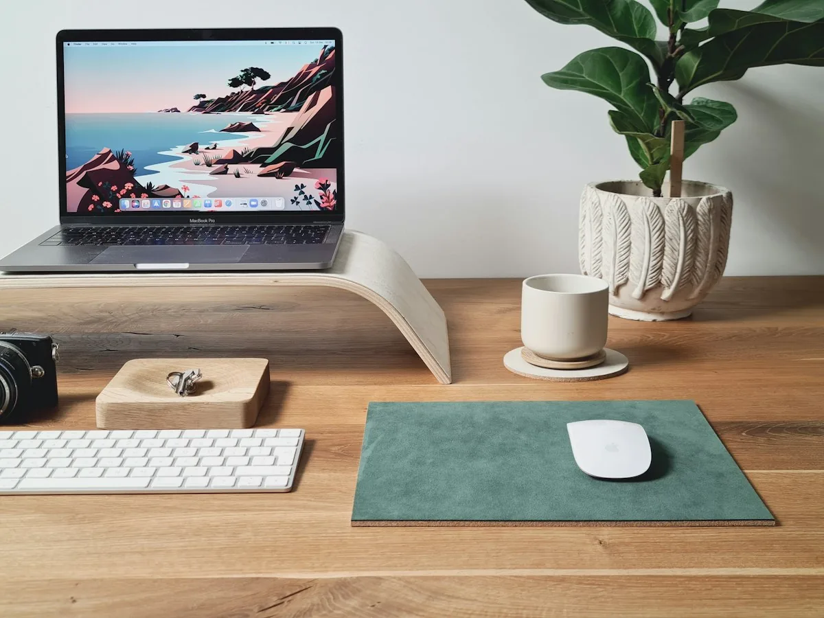 Laptop raised on a wooden stand next to a keyboard and mouse on a desk