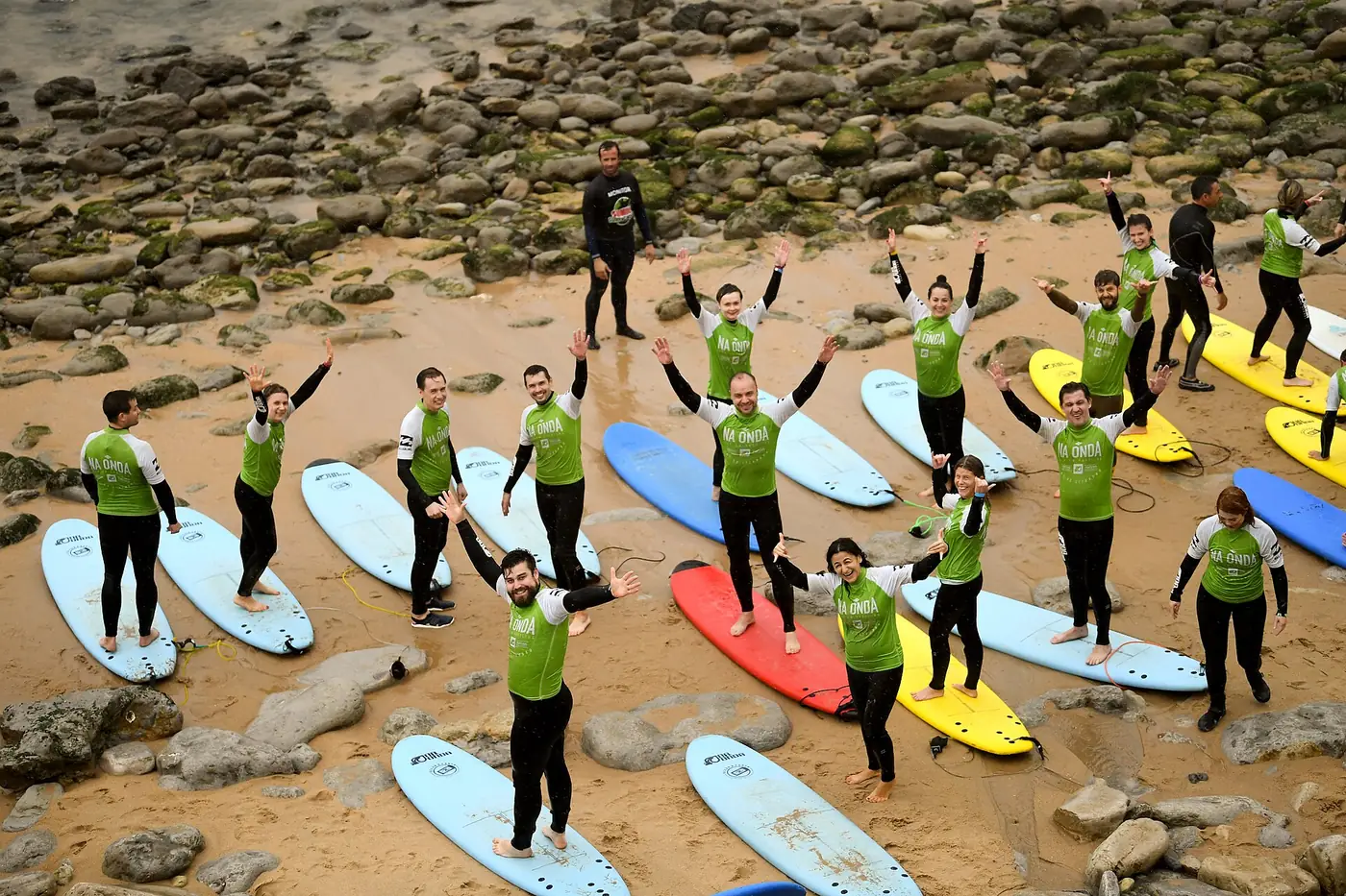 Group of surf students in green tops standing on colorful boards on the beach at Ericeira