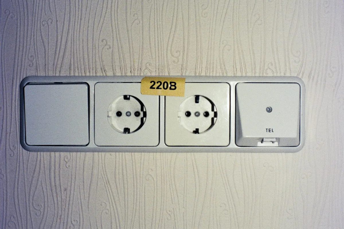 Twee Europese wandcontactdozen met opschrift 220V in een hotelkamer