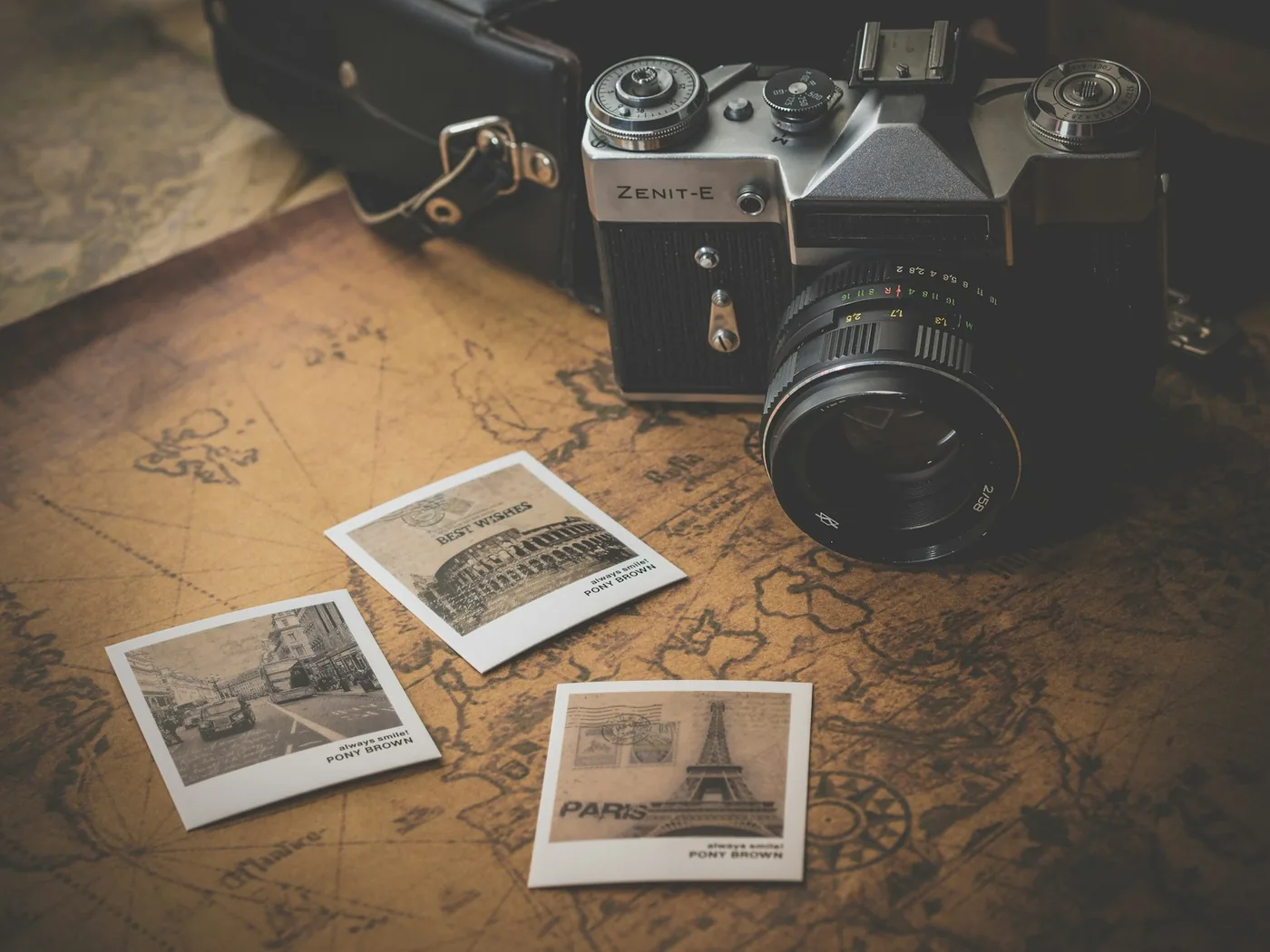 Filmkamera neben drei ausgedruckten Reisefotos auf einer alten Weltkarte