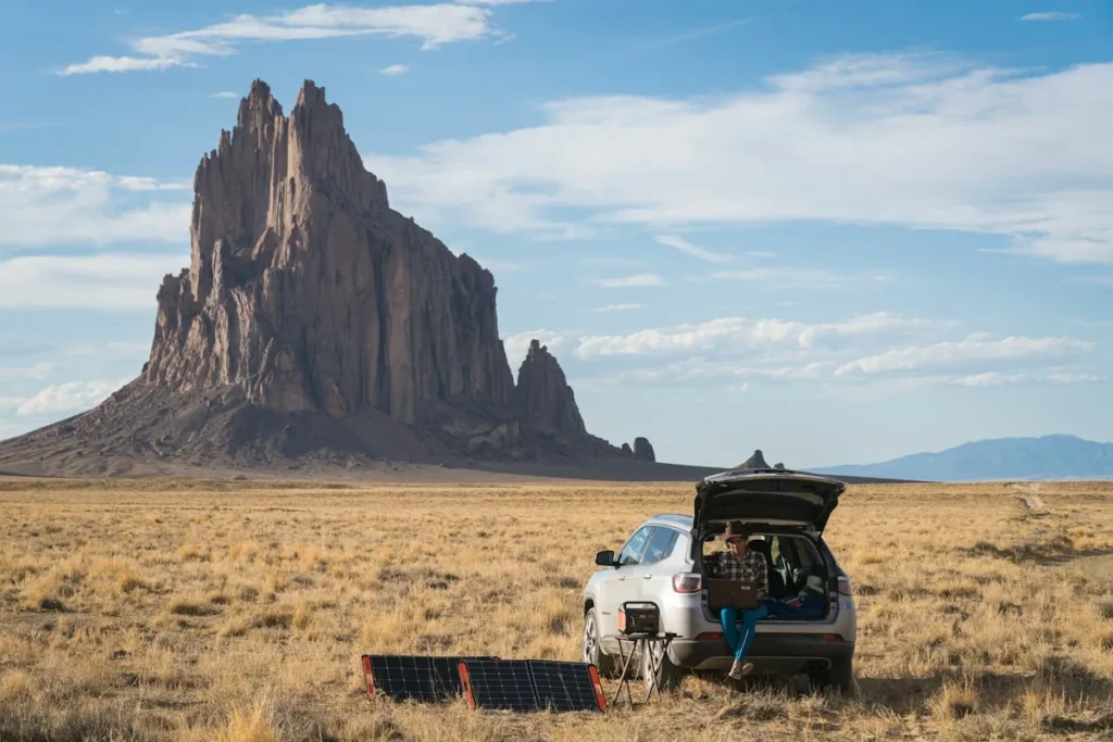 Car with an open trunk and a folding solar panel on the ground in a desert landscape