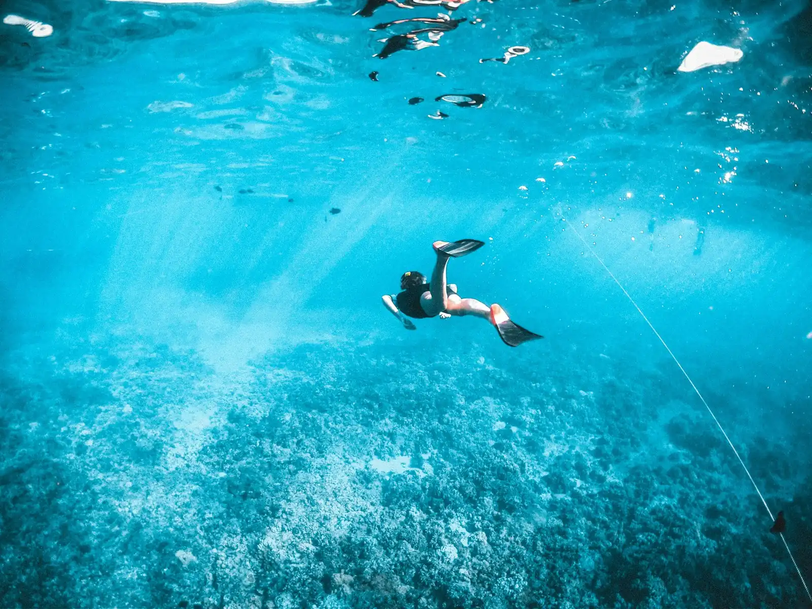 Un buceador libre nadando en agua turquesa con rayos de luz sobre un lecho marino arenoso