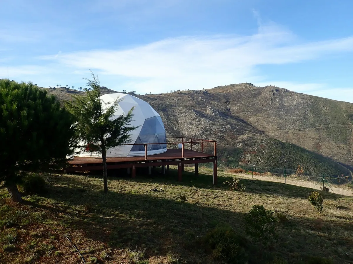 White geodesic glamping dome on a wooden deck on a dry hillside under a blue sky
