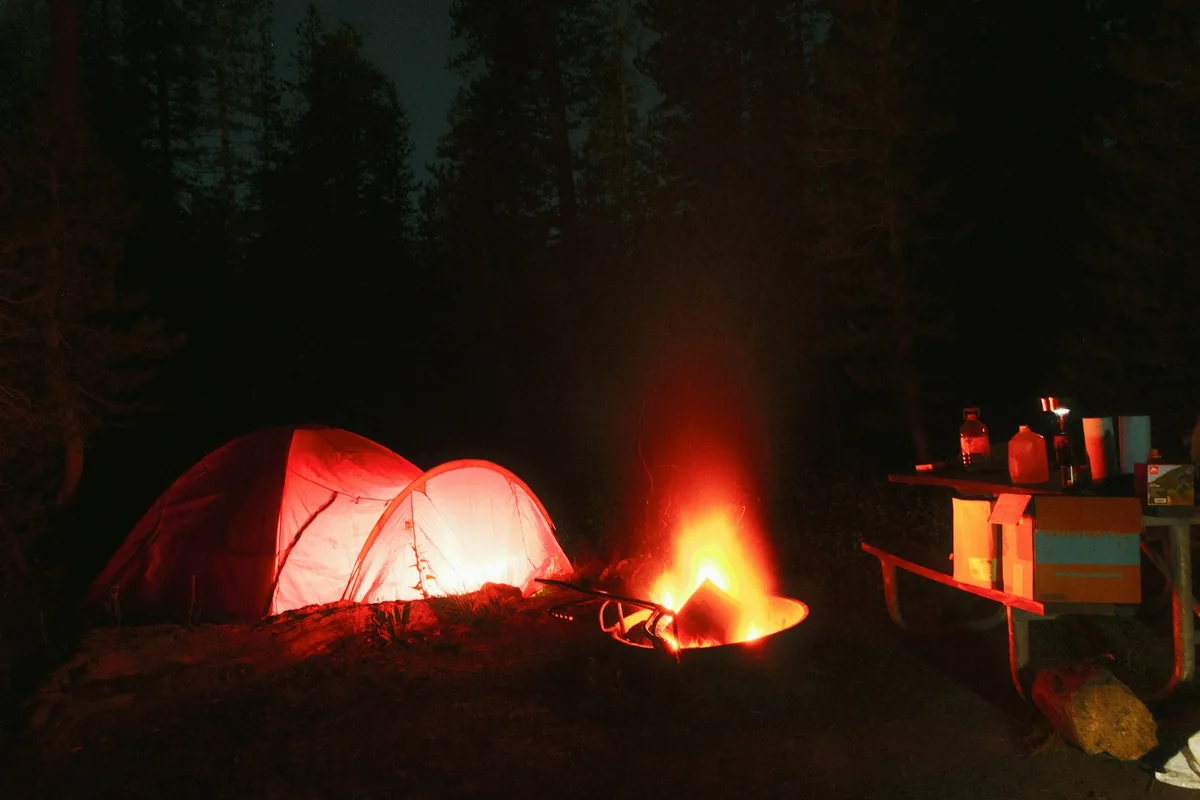 Een gloeiende tent en een kampvuur op een boskampeerterrein in de nacht