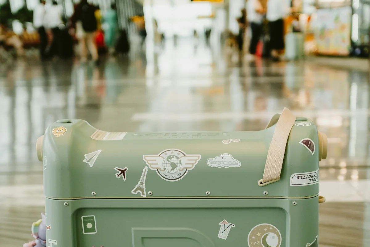 A green hardside suitcase with travel stickers in a bright airport terminal