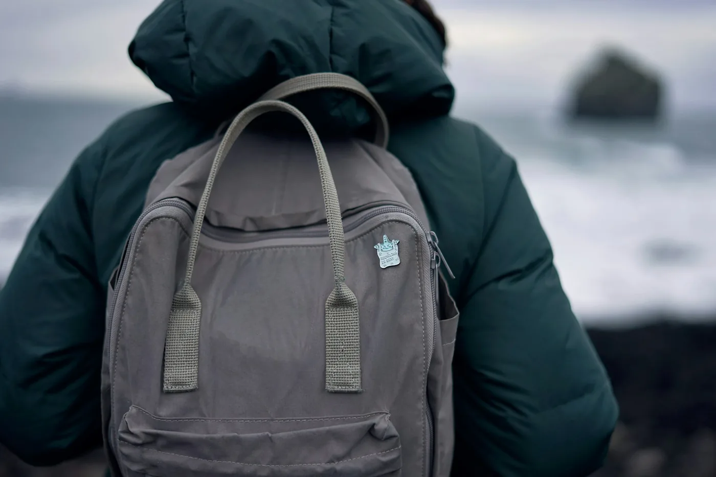 Una mochila de día gris en una persona con chaqueta oscura mirando hacia el mar