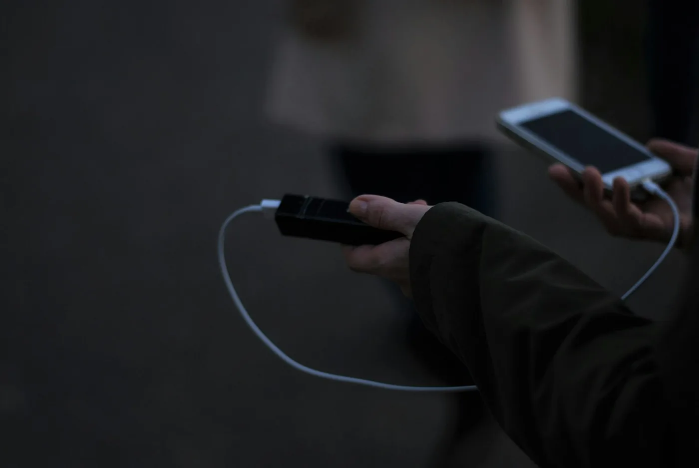Eine Hand hält ein Smartphone, das über ein weißes Kabel von einer kleinen schwarzen Powerbank geladen wird