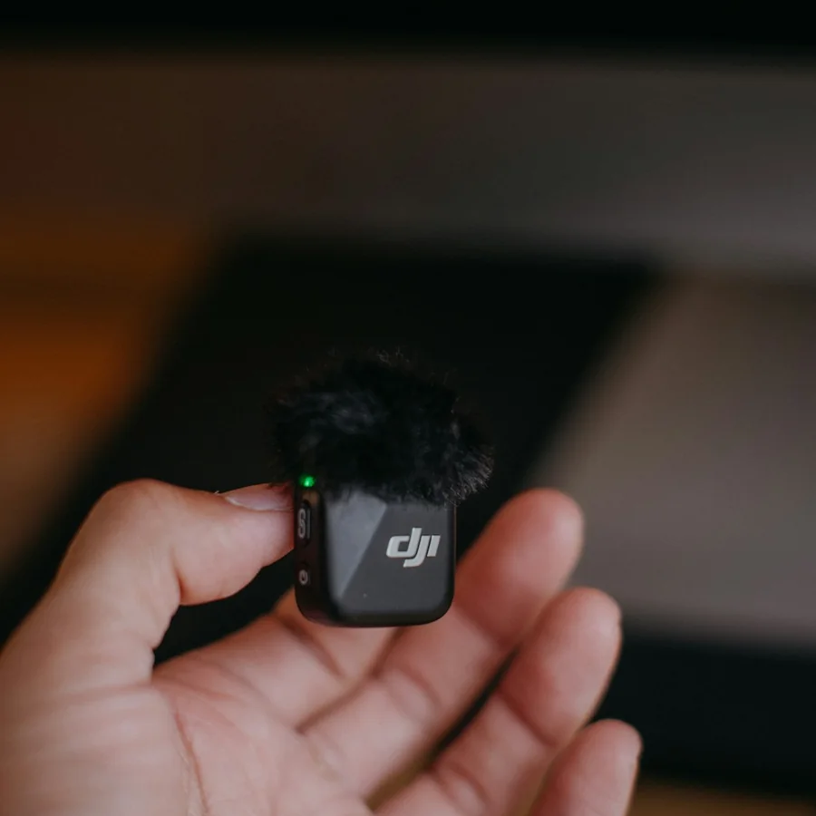 A hand holding a small black DJI clip-on microphone with a furry windscreen