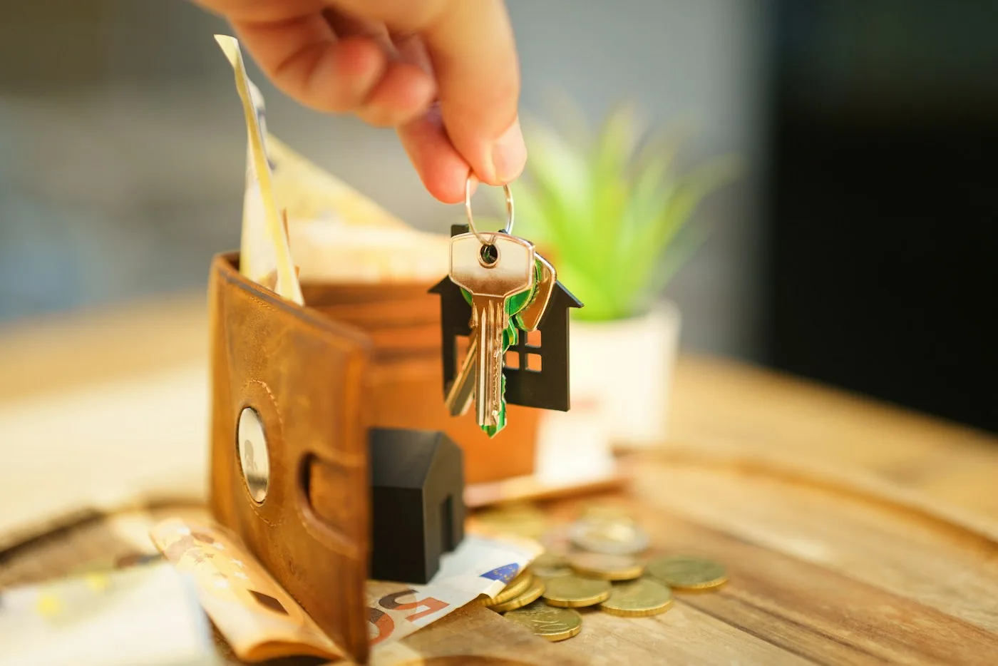 Hand lifting a key with a house charm out of a brown leather wallet