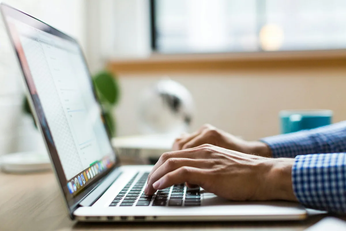 Hands typing on a silver laptop at a bright desk
