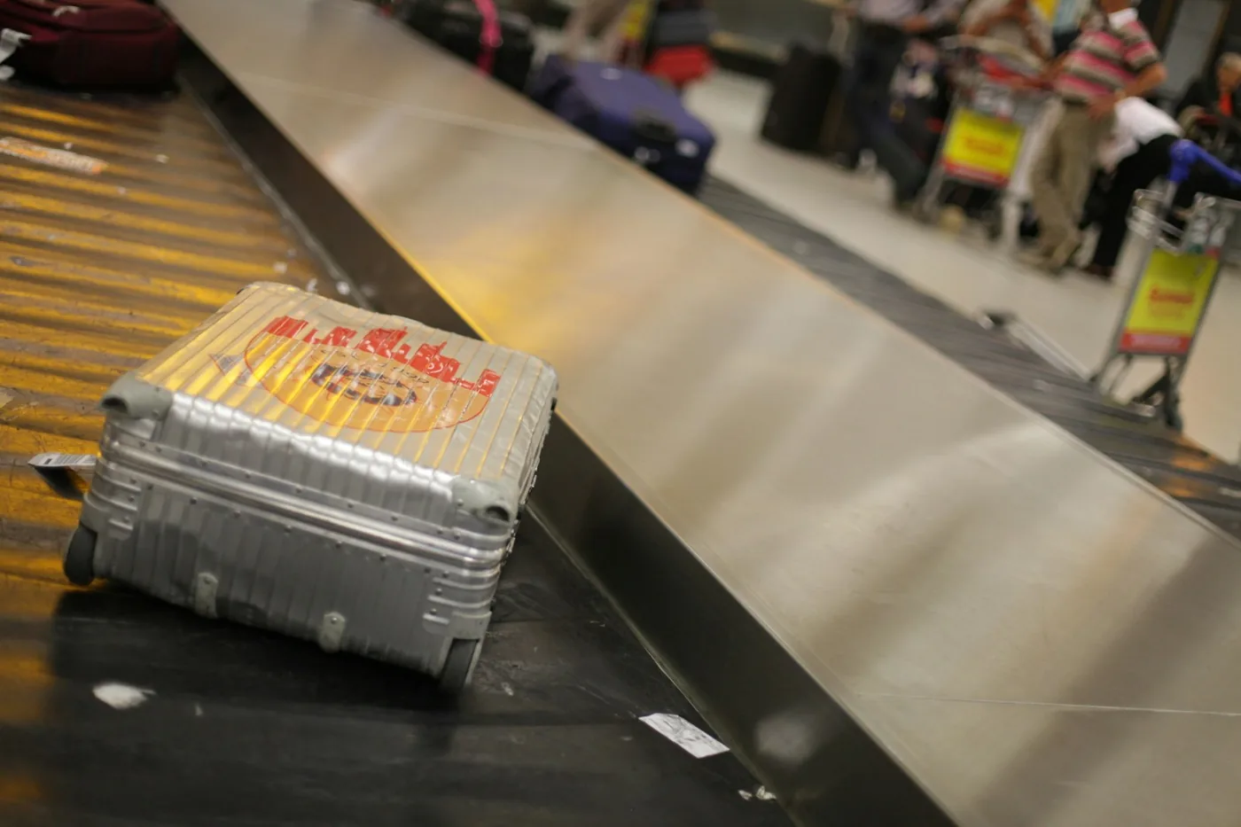 Silver hardside suitcase riding a baggage conveyor belt at an airport