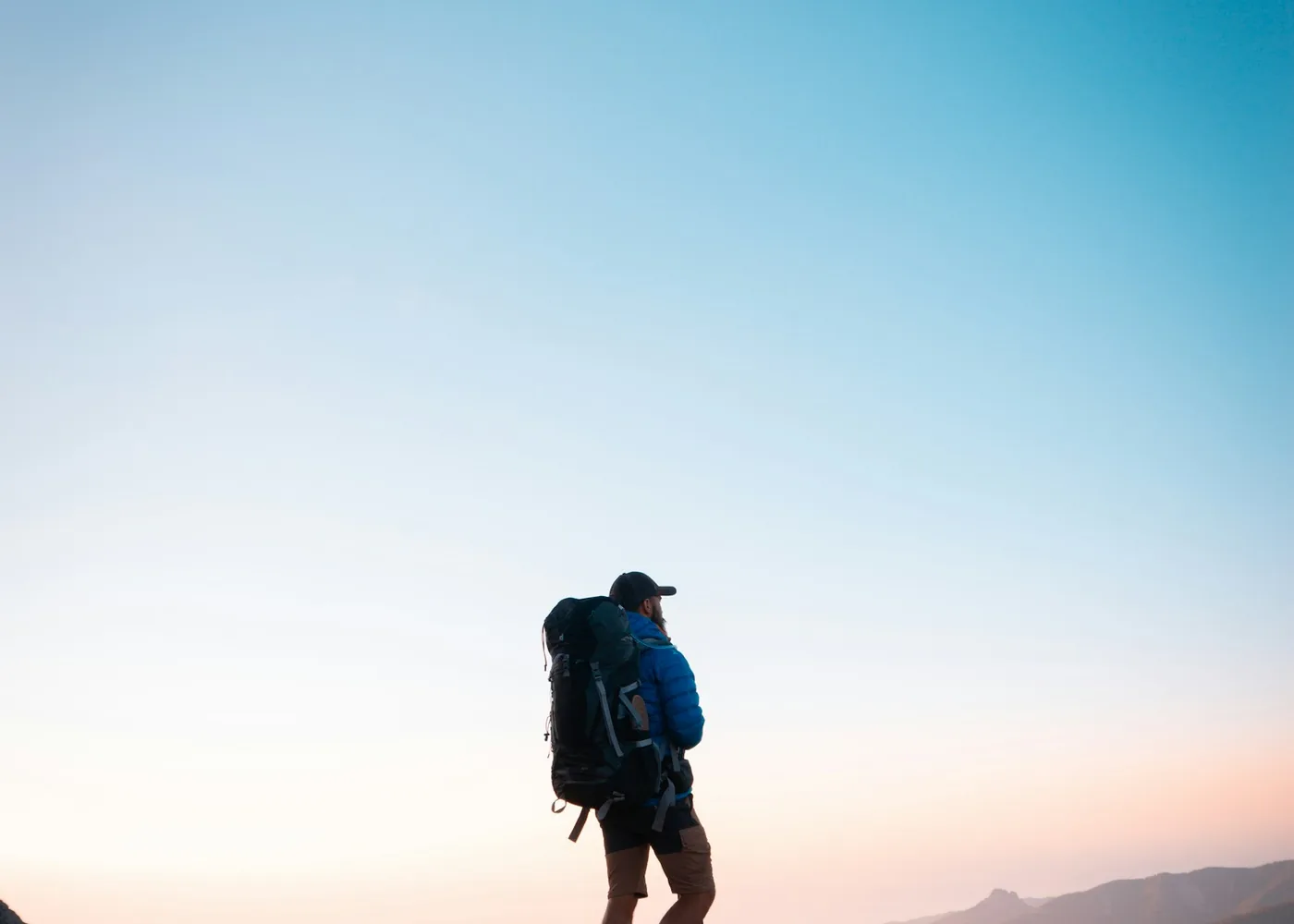 Silhouette of a hiker with a large backpack against a pale evening sky