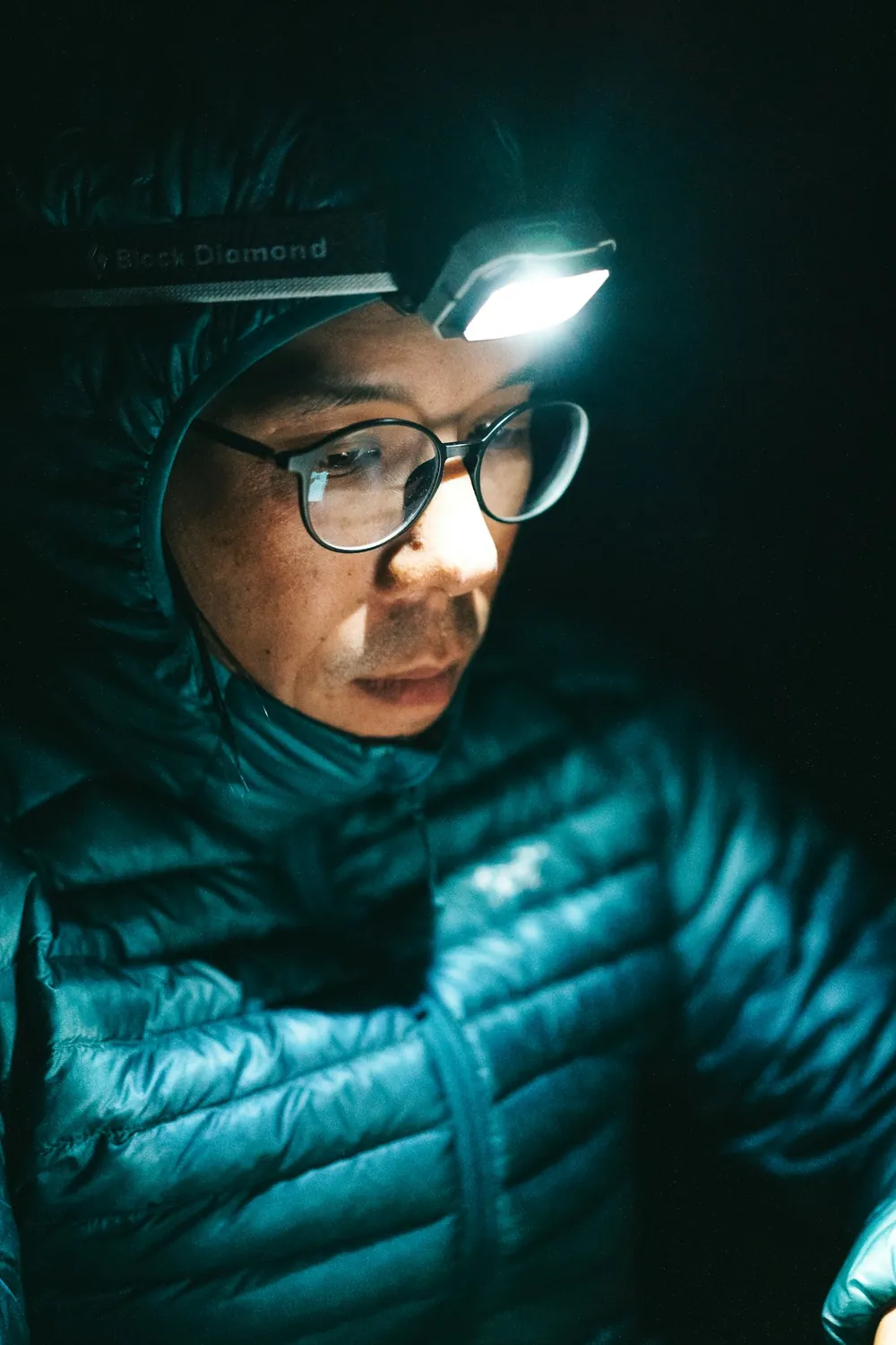Ein Wanderer mit blauer Jacke und Brille trägt in der Dunkelheit eine Stirnlampe