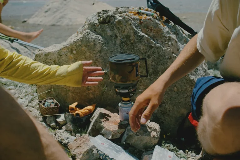 People reaching towards a small camping stove on a rocky surface outdoors