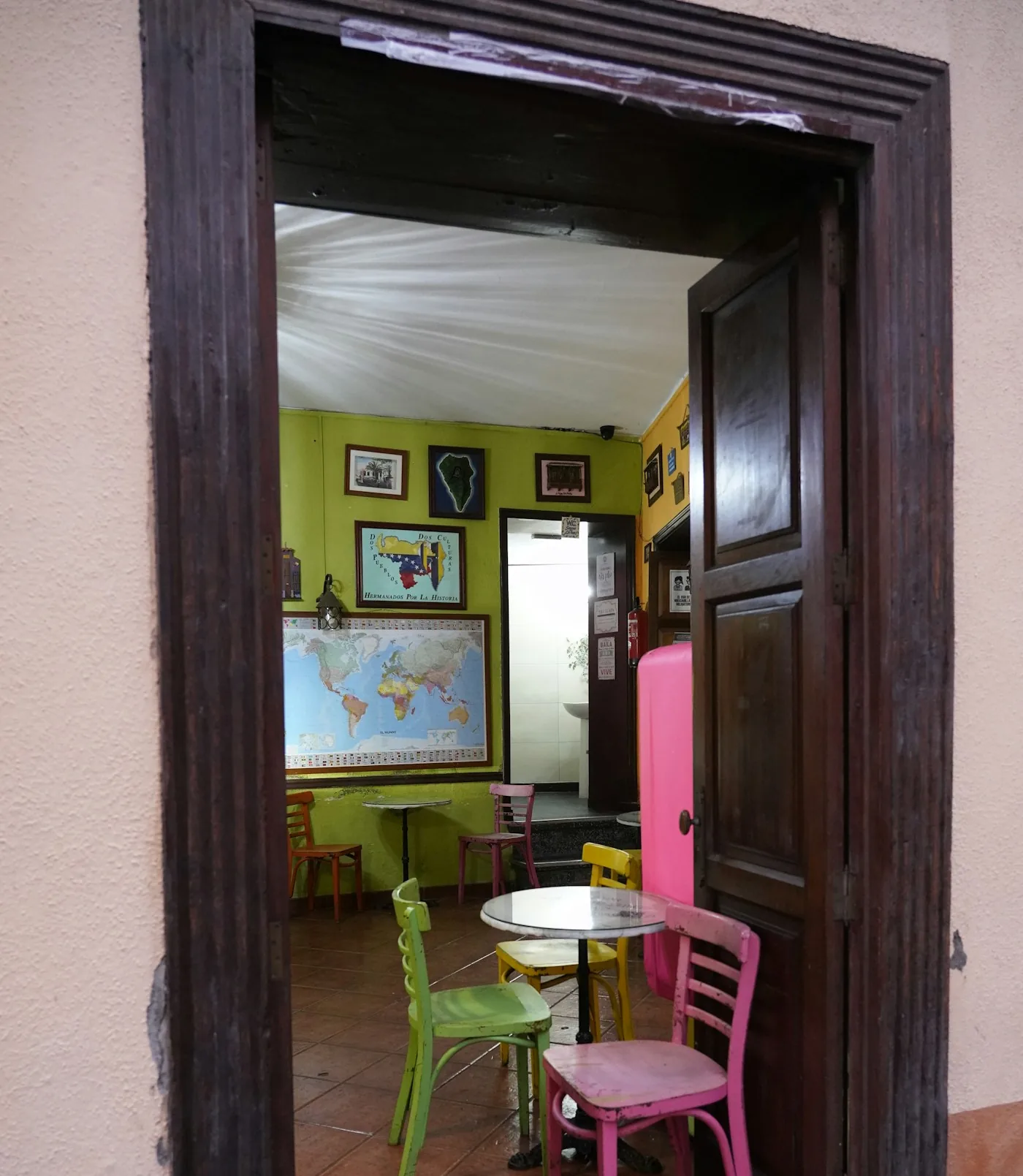 Open doorway to a hostel common room with colorful chairs, a table and a world map on the wall