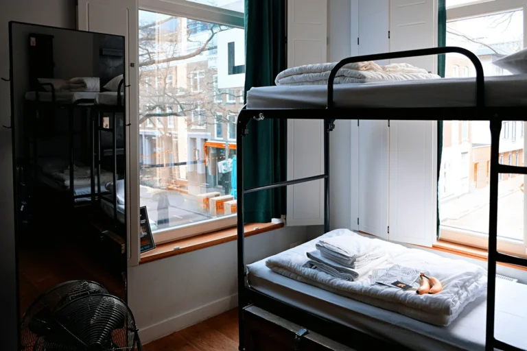 Black metal bunk bed with folded linen in a hostel dorm room by a large window