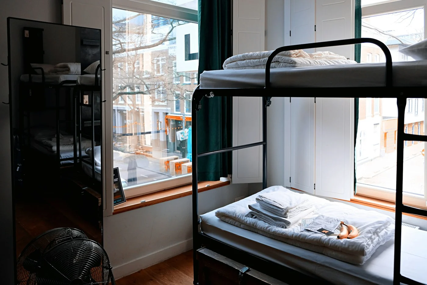 Black metal bunk bed with folded linen in a hostel dorm room by a large window