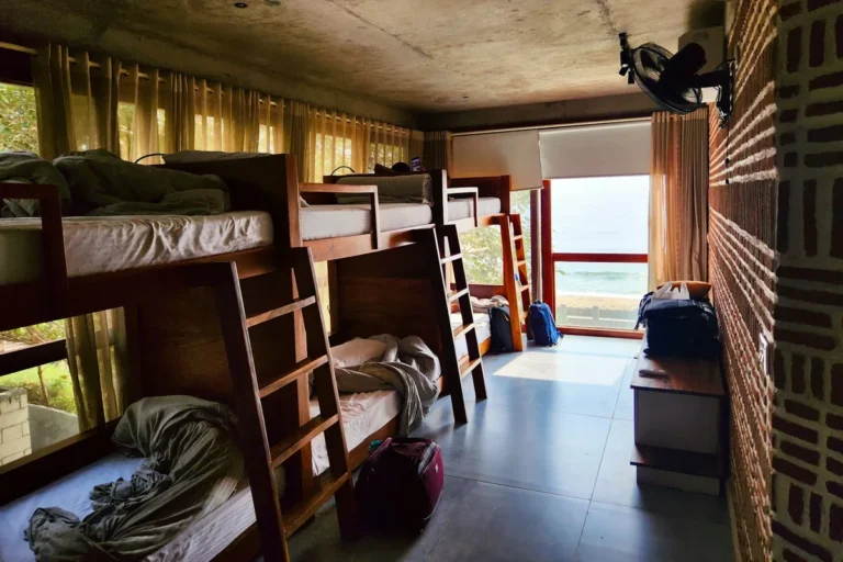 A hostel dorm room with wooden bunk beds and light from a window
