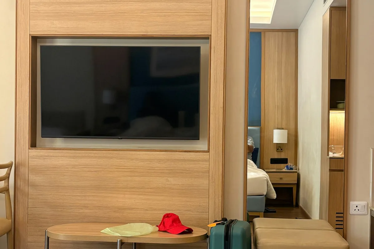 Een hotelkamer met een tv, een spiegel, een koffer en houten meubels