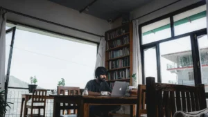 Man working on a laptop at a cafe table by a large window, how to stay productive working from cafes