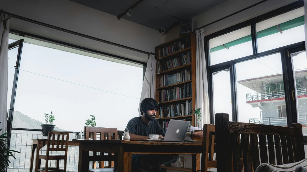 Man working on a laptop at a cafe table by a large window, how to stay productive working from cafes