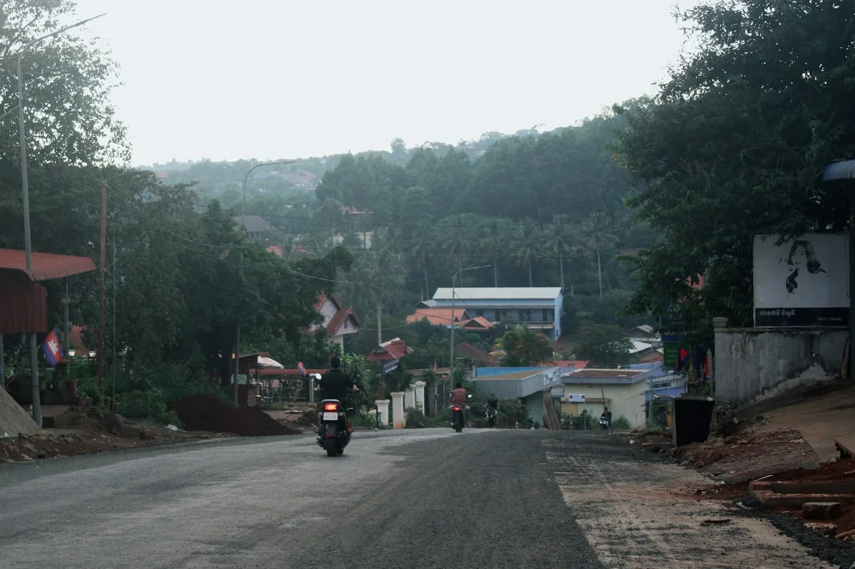 Quiet rural road with green hills and a motorbike in the distance, driving permit in Asia