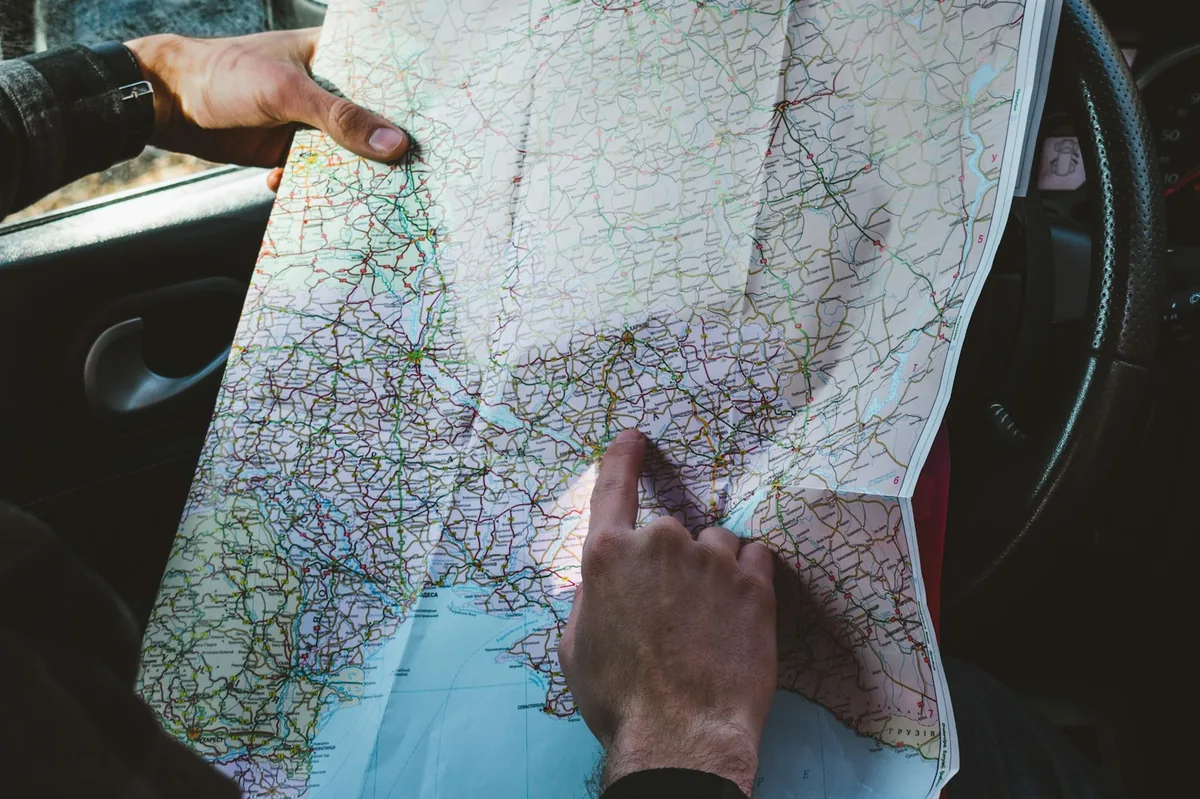 Hands holding a paper road map inside a car, driving permit rules per country