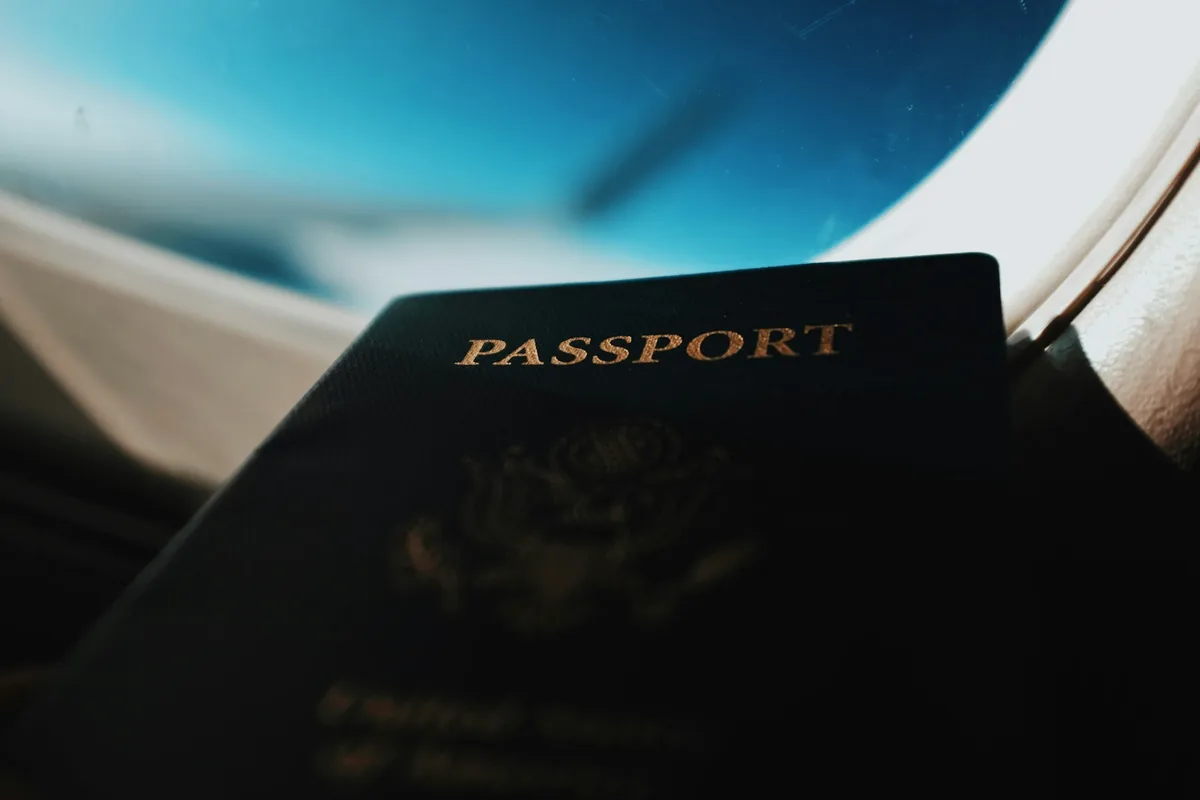 Passport booklet in front of an airplane window, documents for driving abroad
