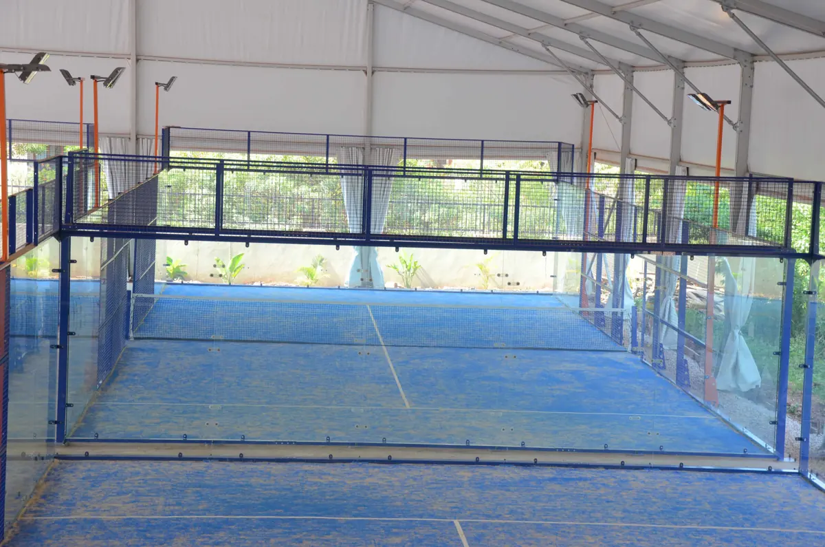 Empty indoor padel court with a blue floor and glass walls