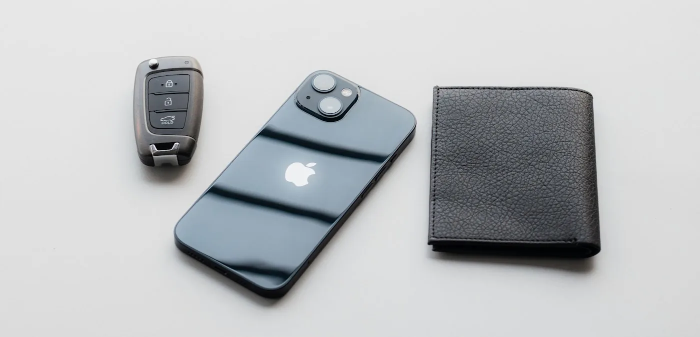 iPhone, a car key fob and a black wallet laid out on a light grey surface
