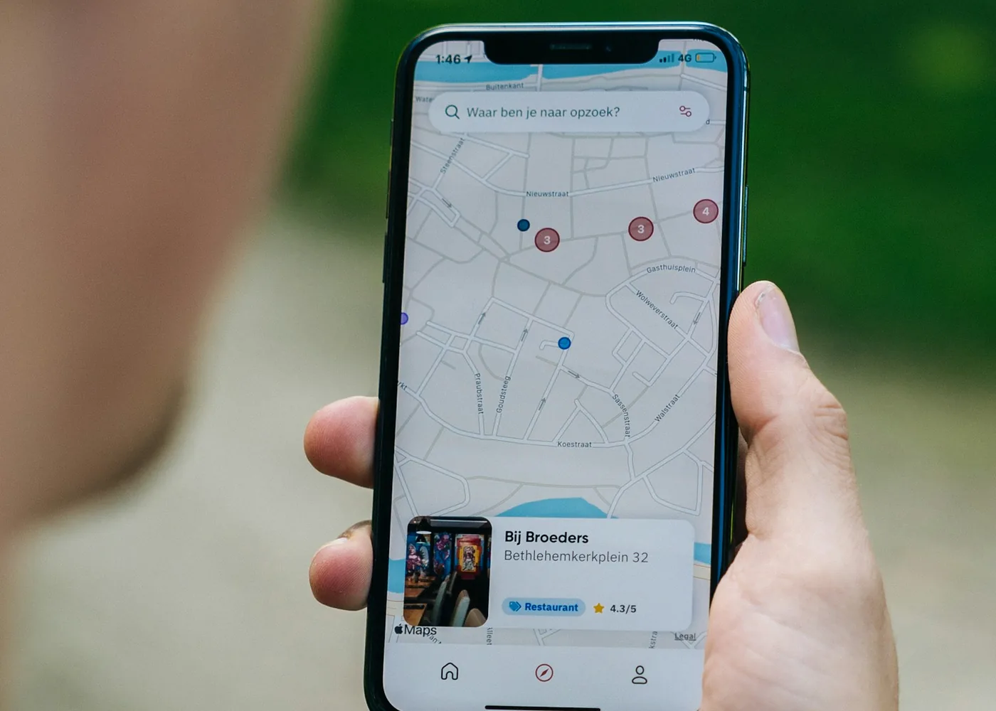 Hand holding an iPhone that shows a map with red pins, like the Find My app does for an AirTag