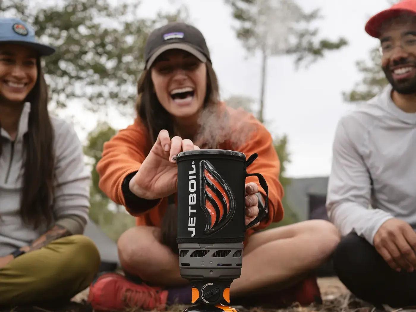Freunde lachen um einen dampfenden Jetboil Flash, der auf einer JetPower-Gaskartusche an einem Campingplatz steht