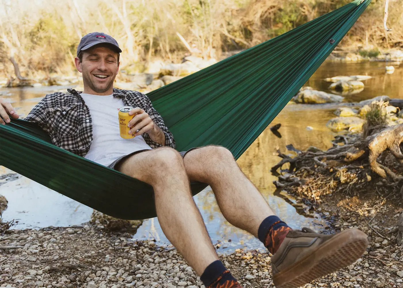 Man lounging in a green Kammok hammock beside a river
