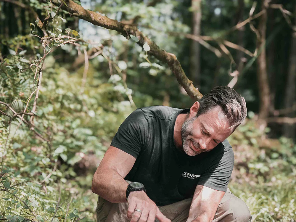 Wanderer in schwarzem Shirt hockt im Wald und füllt eine Katadyn BeFree Flasche aus einem Bach