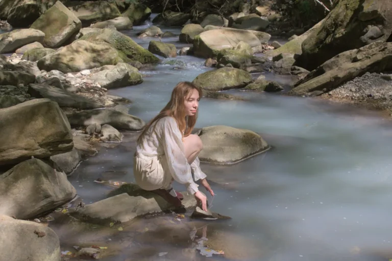 Woman crouching on a rock in a clear mountain stream, where a hiker would filter drinking water