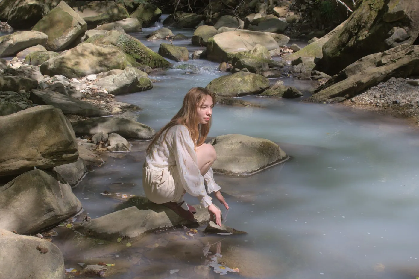 Woman crouching on a rock in a clear mountain stream, where a hiker would filter drinking water