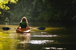 A woman paddling a kayak on a calm river through green forest