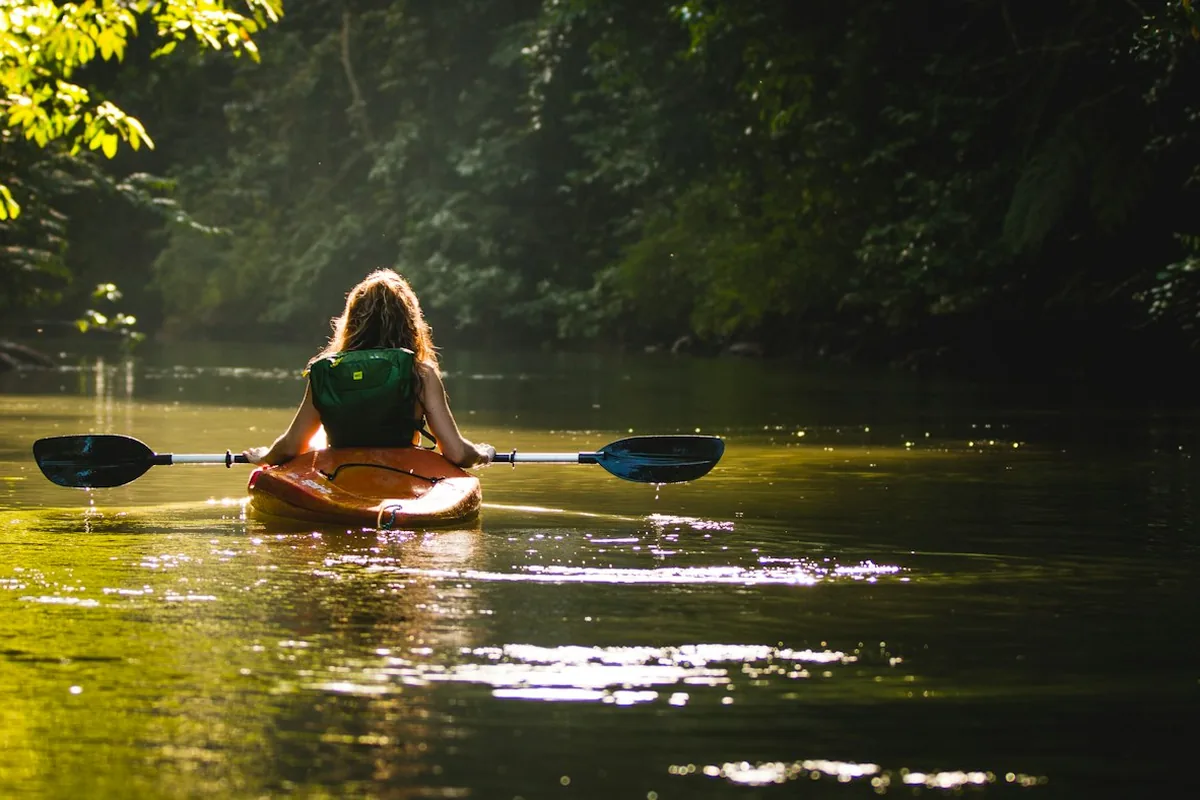 A woman paddling a kayak on a calm river through green forest