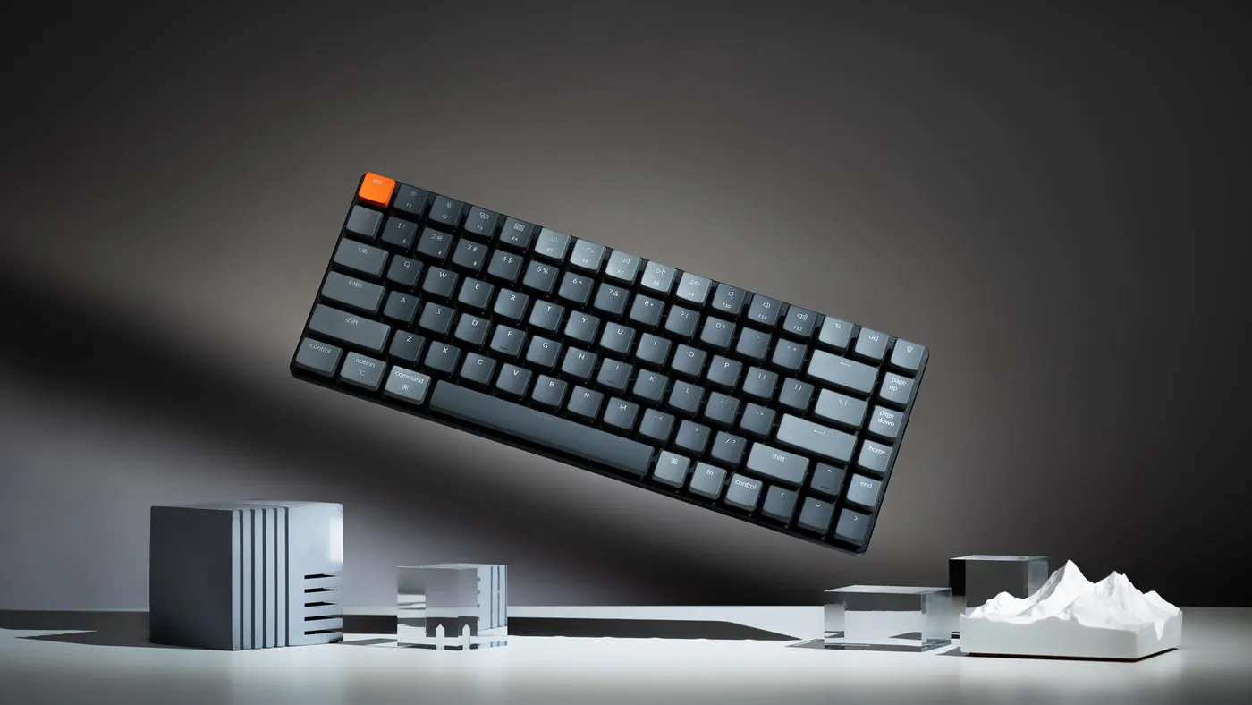 Keychron K3 ultra-slim keyboard tilted in the air above a desk with small gray objects