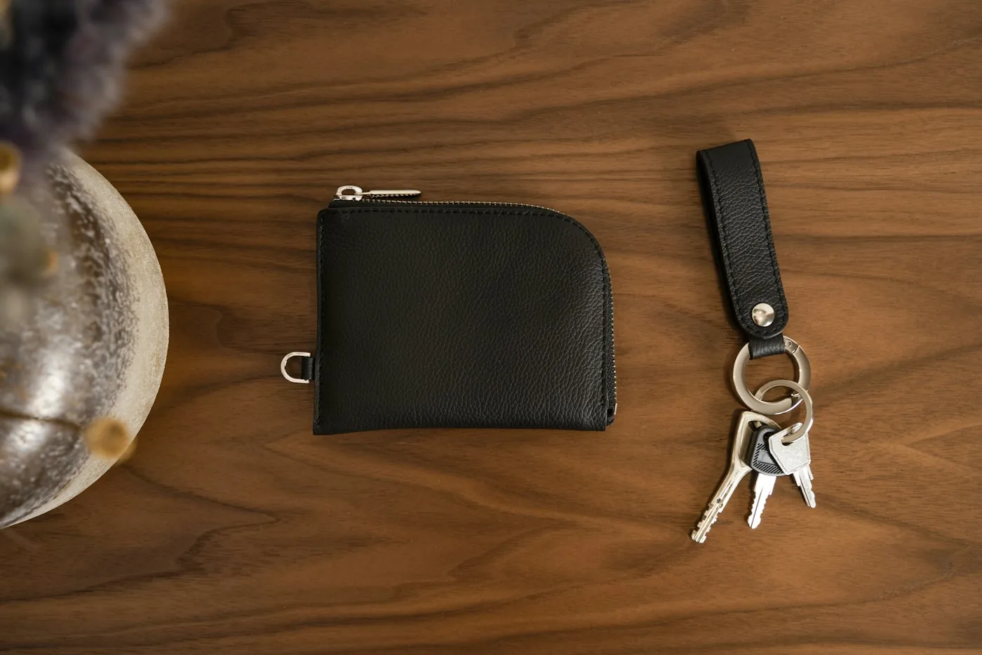Black leather wallet and a key ring with keys on a dark wooden table