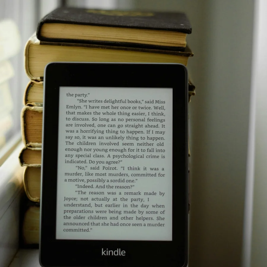 A Kindle e-reader standing on a window sill against a stack of old books
