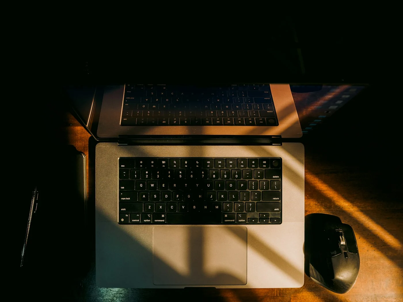 A laptop and a black mouse on a desk with warm sunlight and shadows falling across them