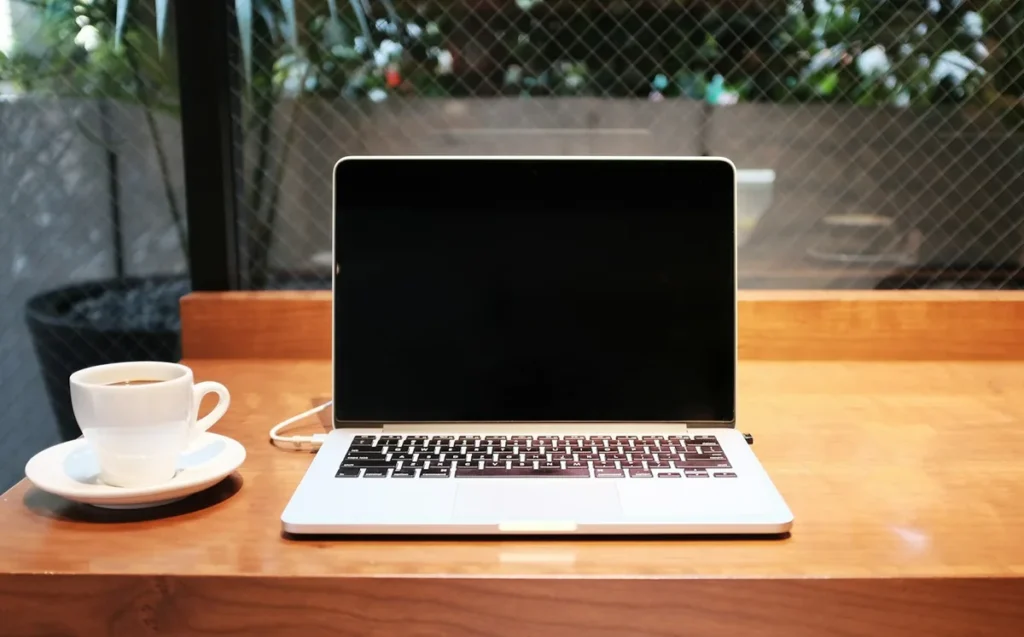 Open laptop and a cup of coffee on a wooden cafe table