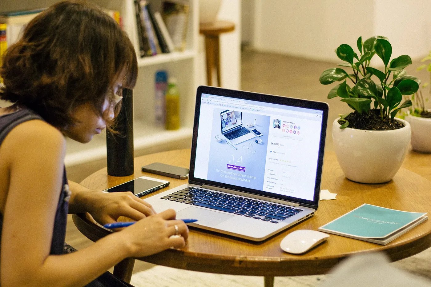 Woman working on a laptop at a round cafe table with a notebook and a plant, the kind of spot where a portable monitor earns its place